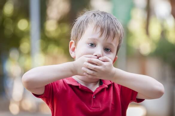 Menino cobrindo a boca com as mãos, evitando falar.